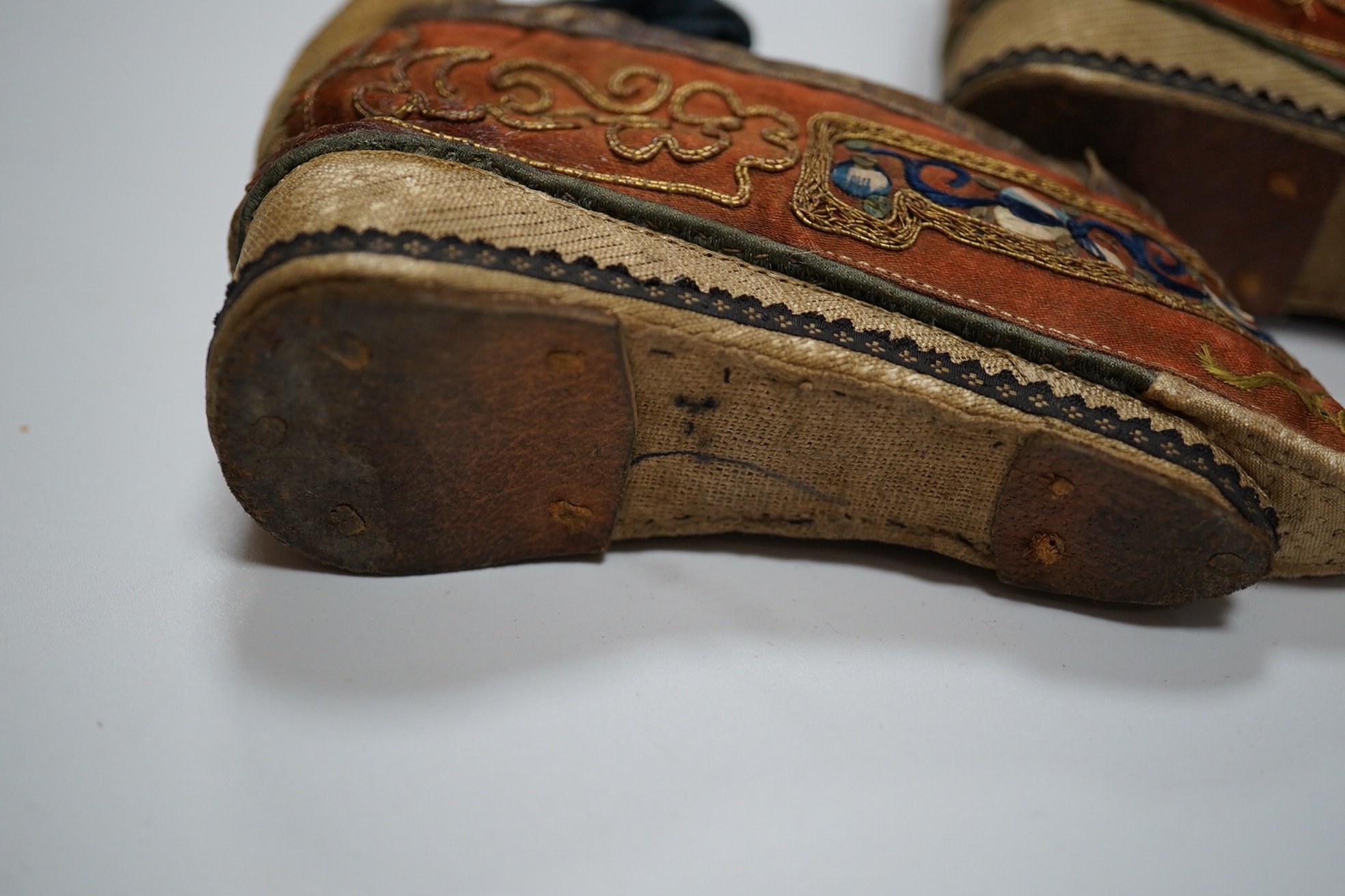 A pair of Chinese silk and gold thread embroidered ladies shoes, with leather binding around the top and gold brocade platform heels with fine blue braiding, 12cm long. Condition - good for age and use